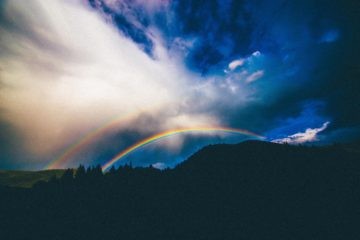 Two rainbows surrounded by clouds near mountains